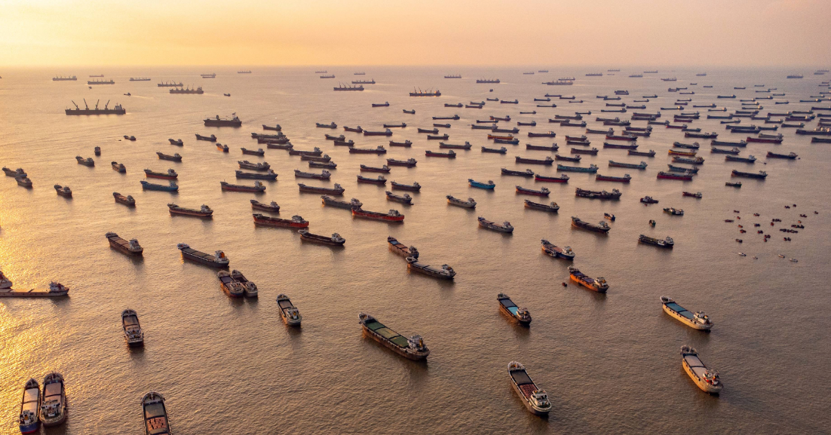 a fleet of anchored cargo ships on placid water at sunset