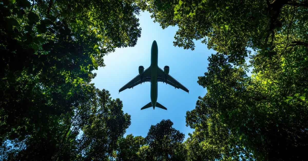 An aerial view of an airplane using sustainable aviation fuel, flying over a forest.