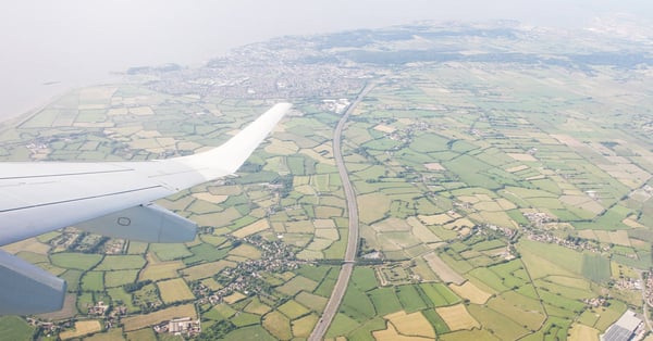 The wing of an airplane flying high over fields and crops.