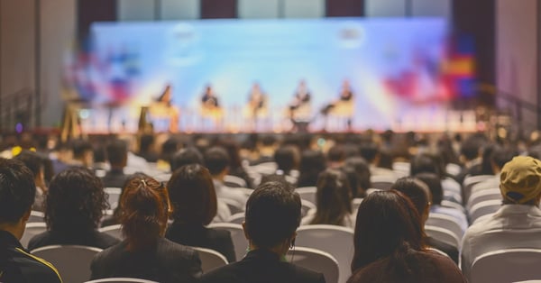 A large audience gathered in a conference hall with several presenters on stage.
