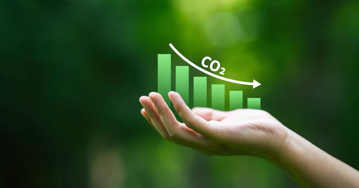 A hand holding a lowering bar chart, indicating CO2 is decreasing.