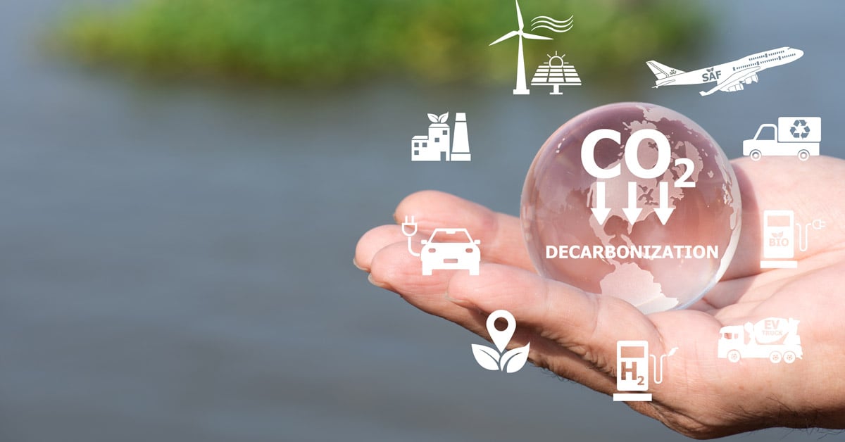A hand holding a global with a downward arrow and CO2, indicating decarbonization.
