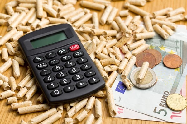 A calculator sitting atop some paper euros and wood pellets, indicating the cost of biofuel production.