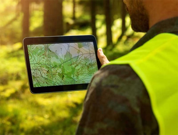 A forester out in the woods looking at a relief map of their timber stand. 