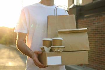 Young man carrying several bags and cups in a carrier, all made out of paper instead of a non-biodegradable material.