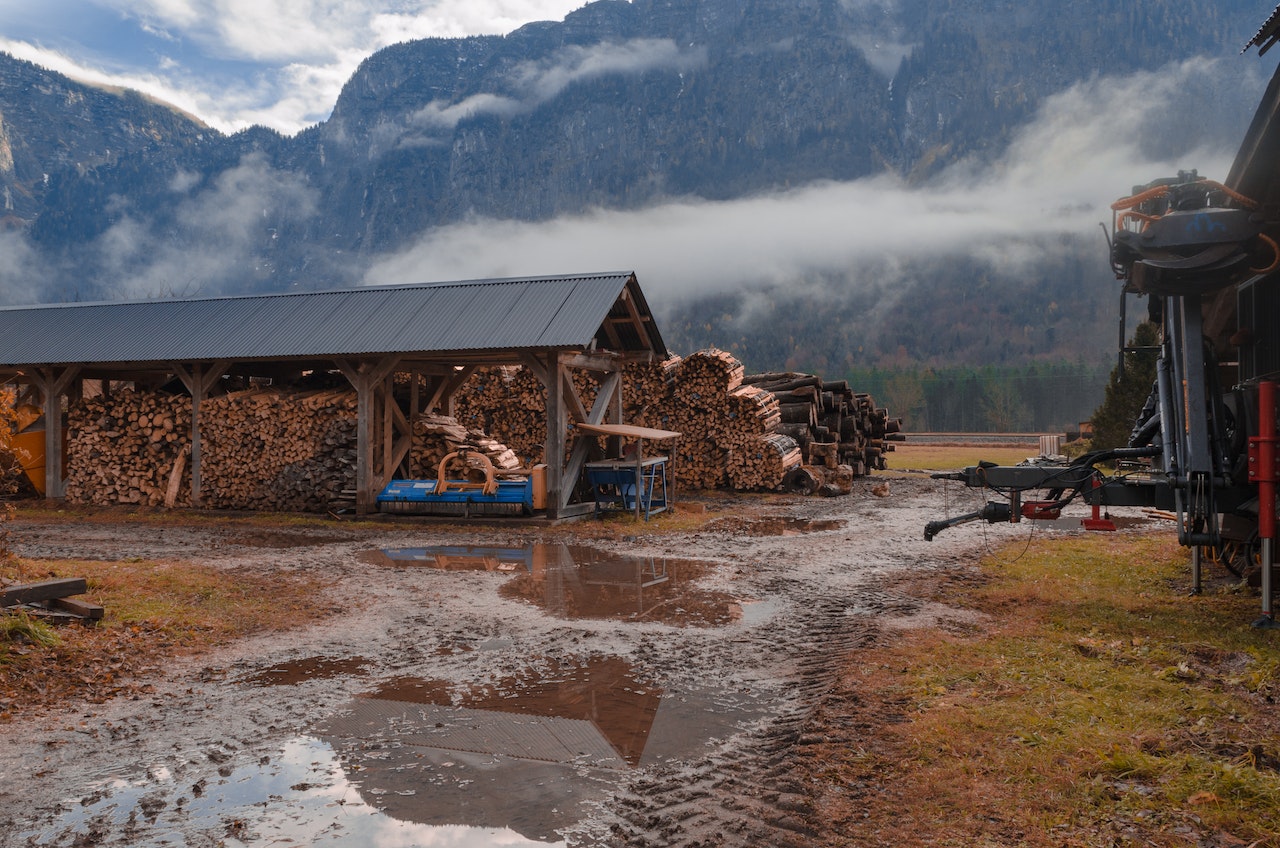 A small saw mill sits below a spanning mountain range with wispy clouds passing by.