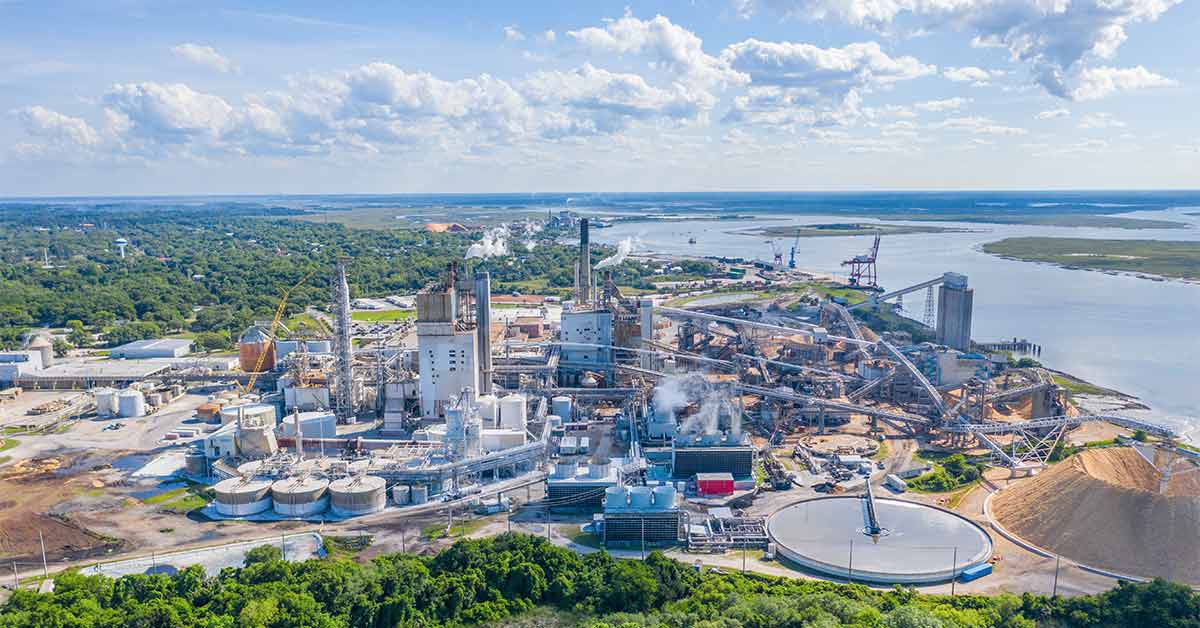 Outside overview of a paper mill near a port in Florida with a large chip pile near the mill machinery.