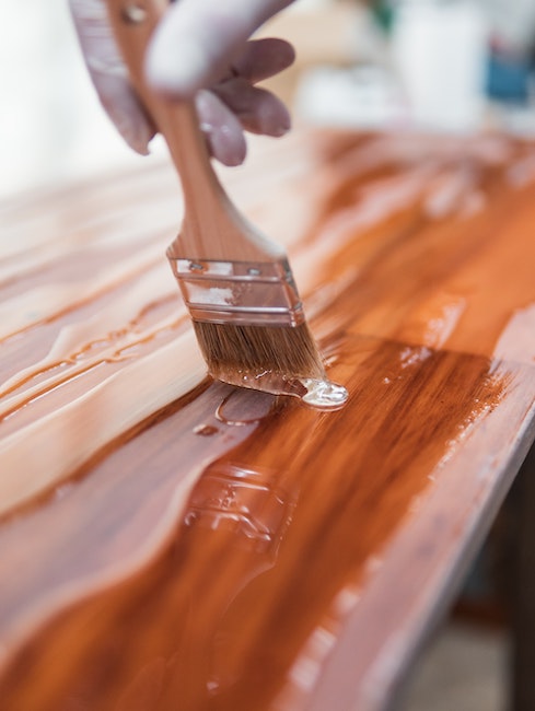 Someone holding a paintbrush using acrylic to finish a piece of wood. 